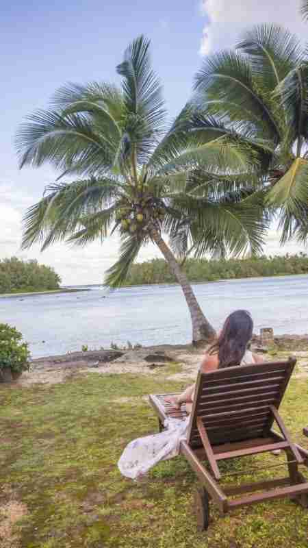 Girl relaxing on sun chair waiting for sunset with palm trees and Muri Lagoon in the background