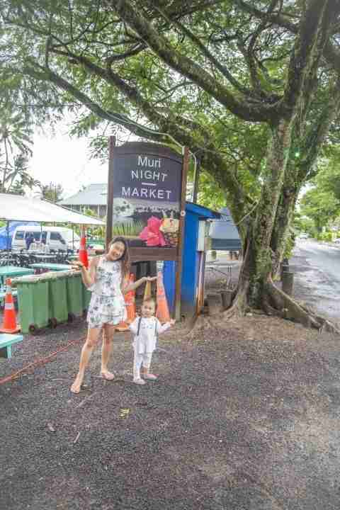 Mommy and daughter shrugging in front of Muri Night Market sign that no one is here on a rainy day and empty stalls