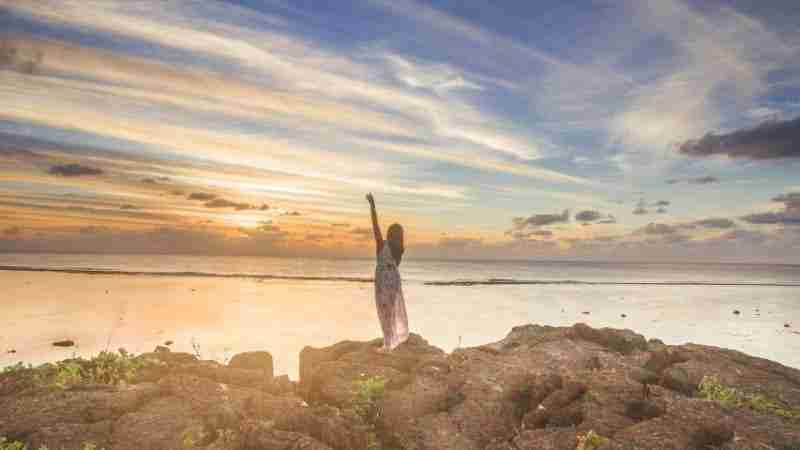 Girl touching heaven standing on top of black rock chimneys of Rarotonga at sunset